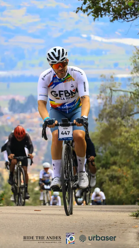 Un ciclista sube por una carretera con otros detrás; al fondo, el valle y las montañas