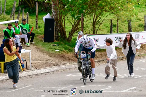 Un ciclista sube una cuesta mientras un niño y dos mujeres corren a su lado, animándolo