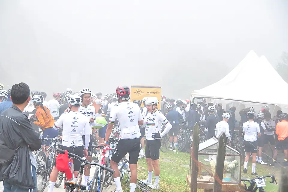 Ciclistas descansan junto a las carpas de una zona de hidratación, entre la niebla.