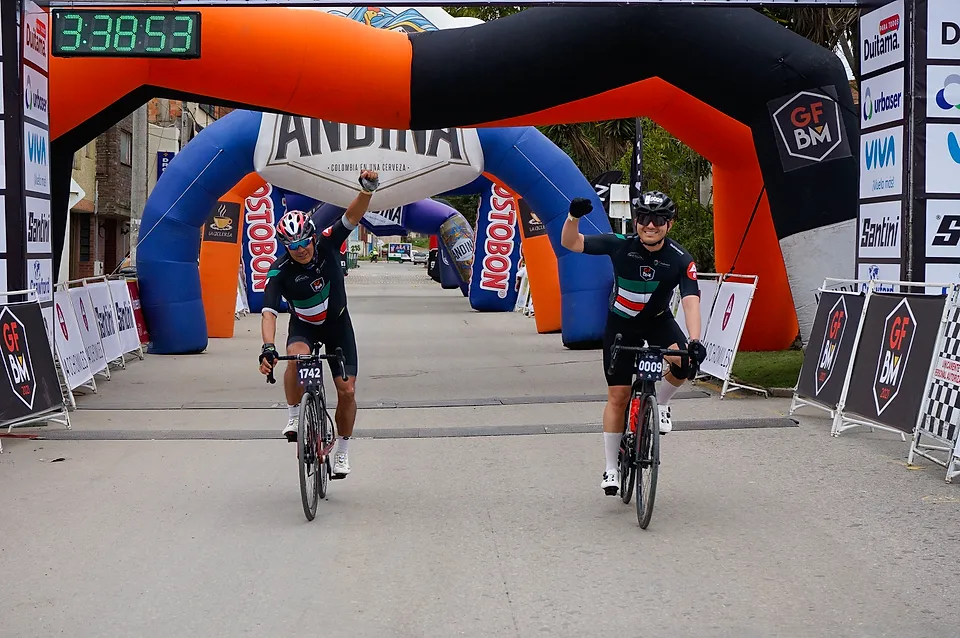 Dos ciclistas cruzan el arco celebrando con los brazos arriba