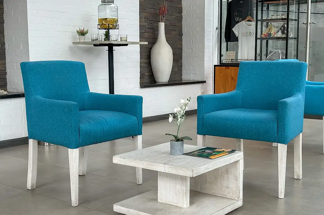 Two blue armchairs around a low pale-wood table in the hotel lobby, against white-painted brick walls.