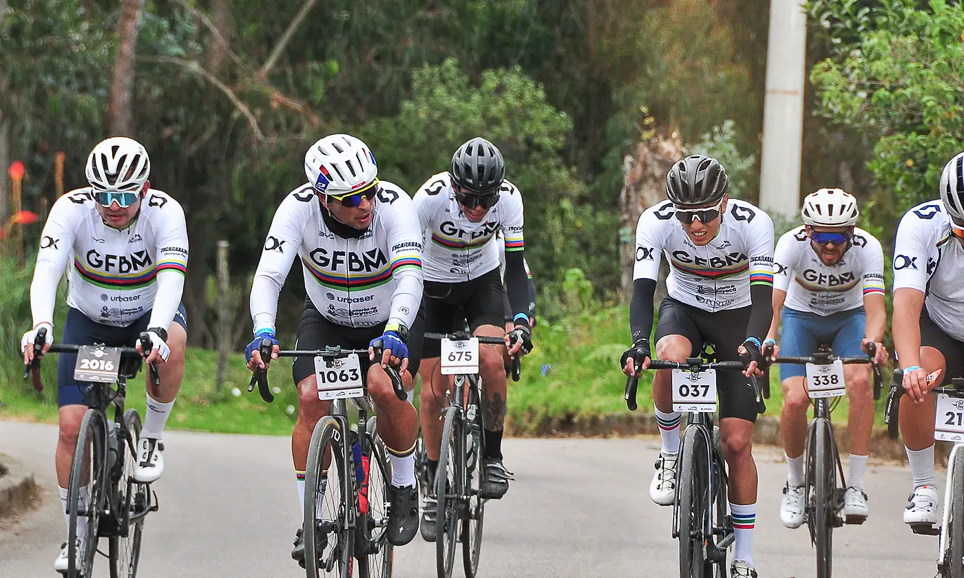 Un grupo de ciclistas con el maillot del evento rueda en llano, en paralelo y conversando.