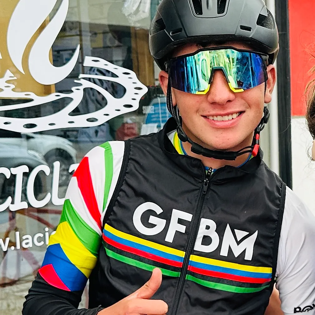 A rider in a Gran Fondo vest, helmet and glasses gives a thumbs up outside La Ciclería