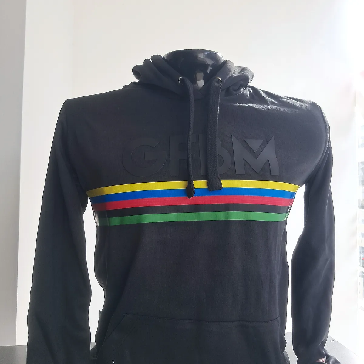 Black hooded sweatshirt of the 2025 edition, with rainbow bands across the chest and the GFBM logo