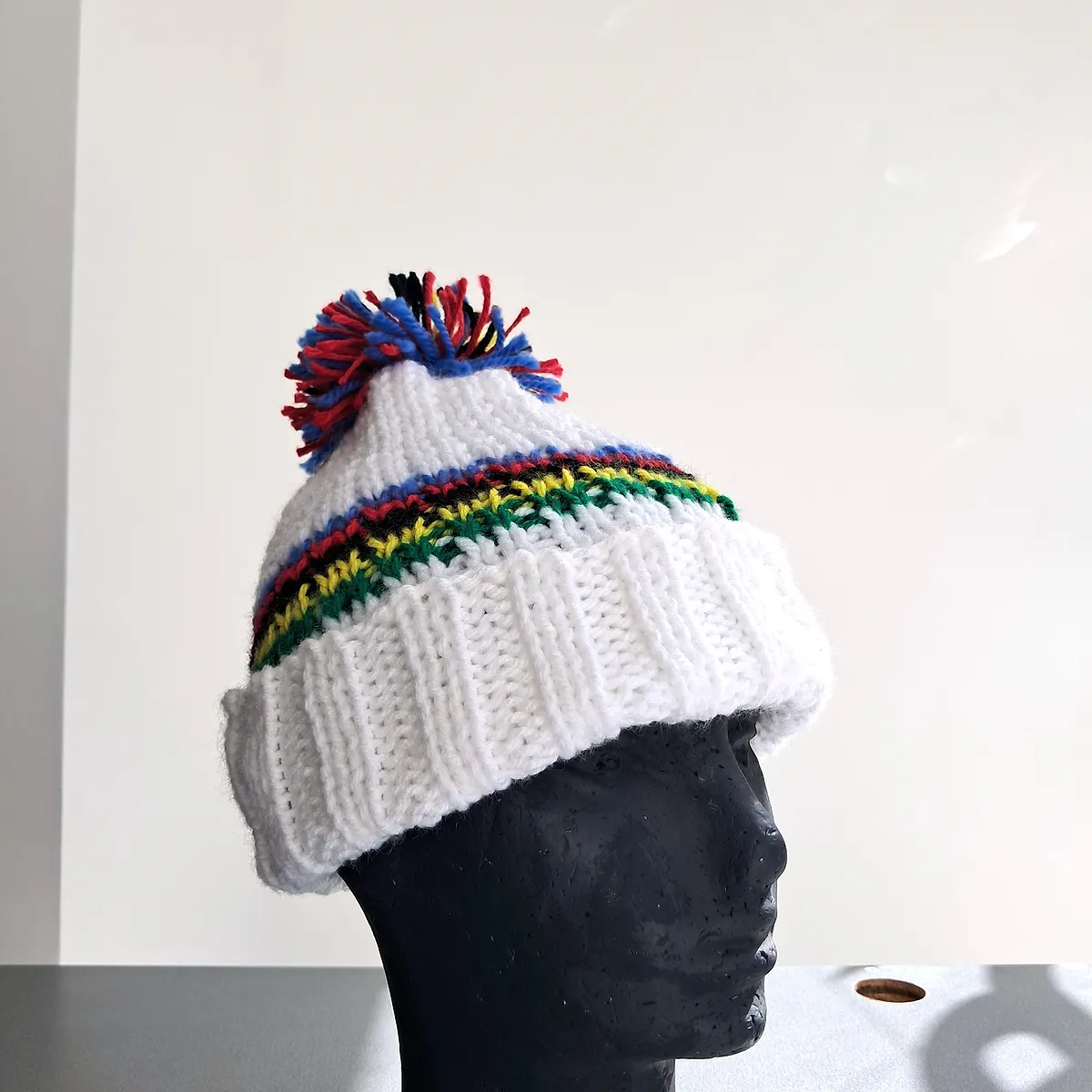 White knitted wool beanie with rainbow bands and a multicoloured pompom