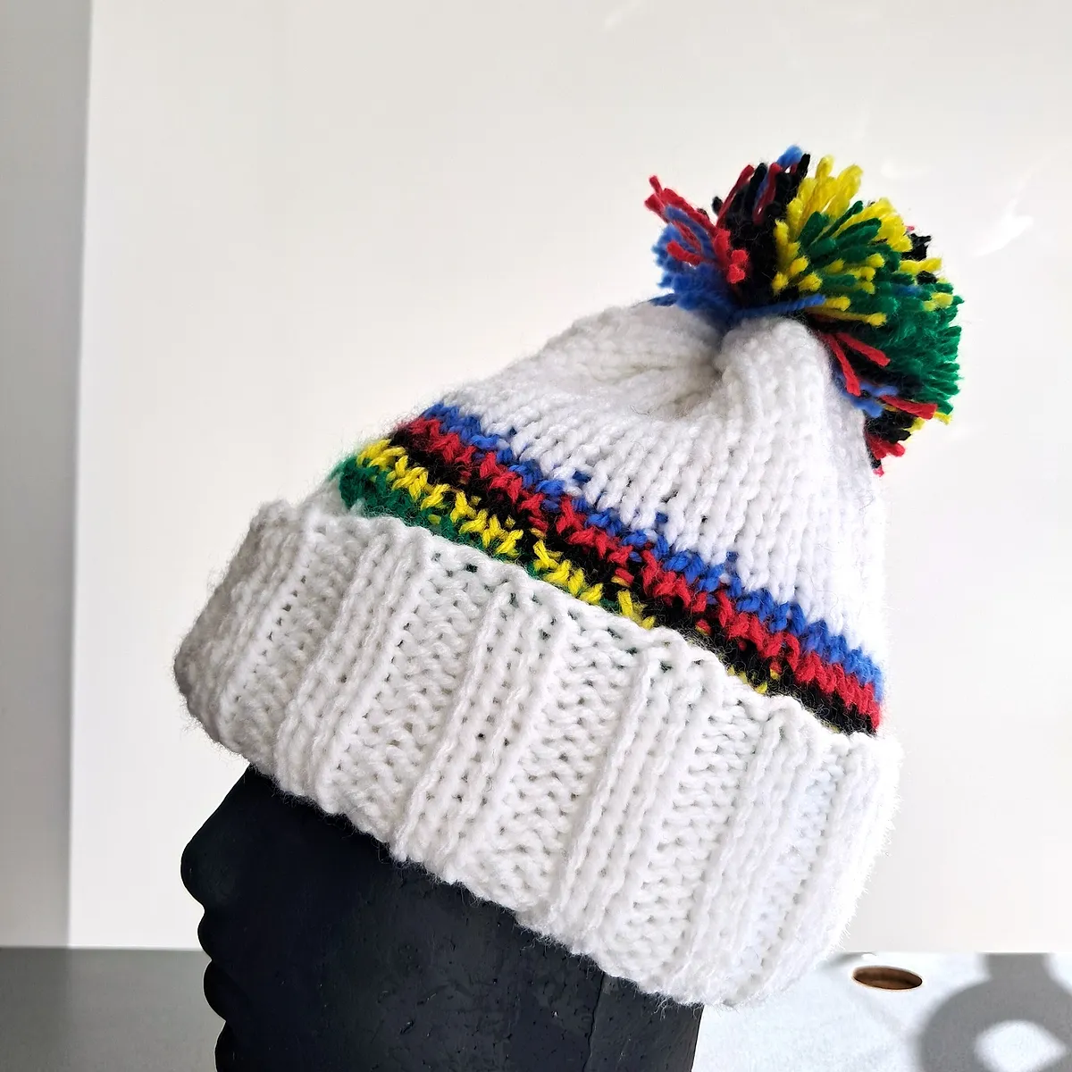 White wool beanie in profile, with the knitted cuff and multicoloured pompom