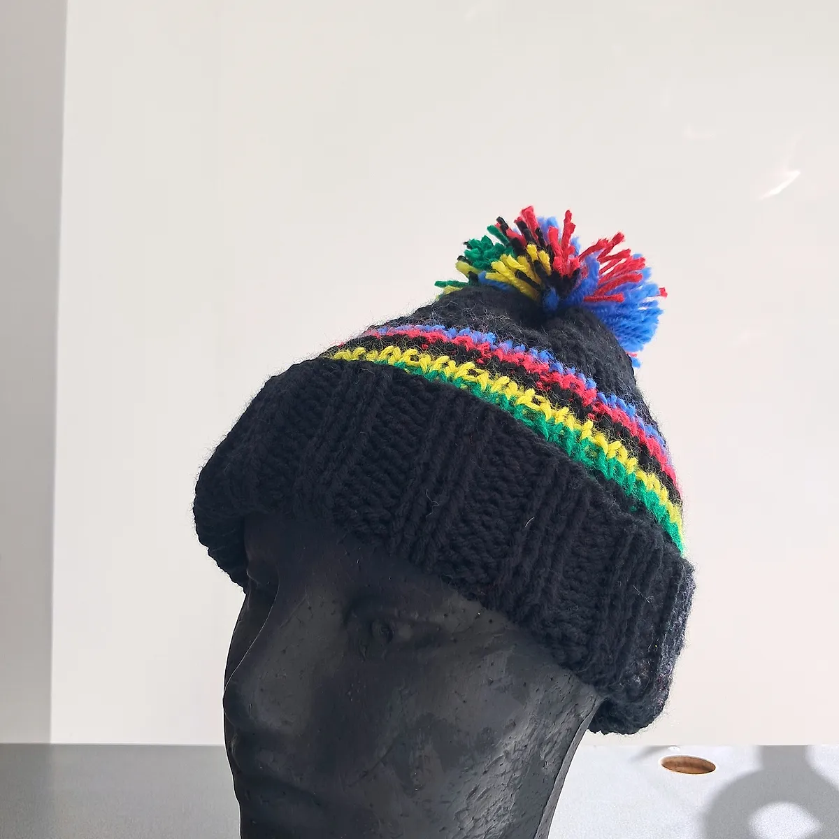 Black knitted wool beanie with rainbow bands and a multicoloured pompom