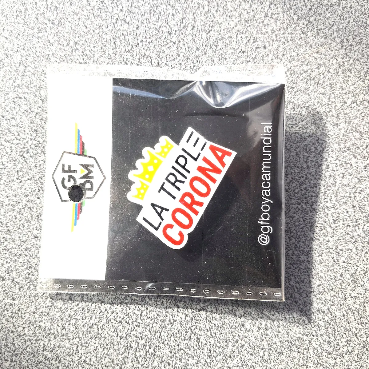 Commemorative pin of the 2018 edition, La Triple Corona, on a black background