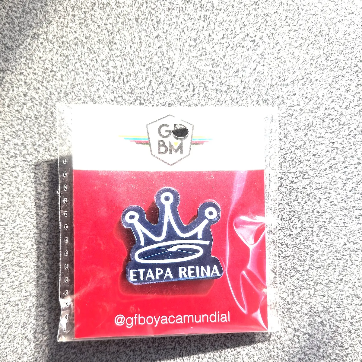 Commemorative pin of the 2023 edition, Etapa Reina, with a crown on a red background