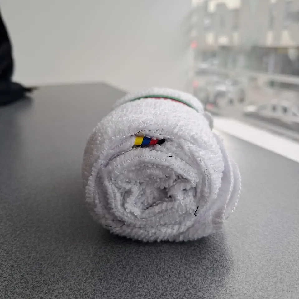 Small white GFBM towel rolled up on the table, with the colour tag showing
