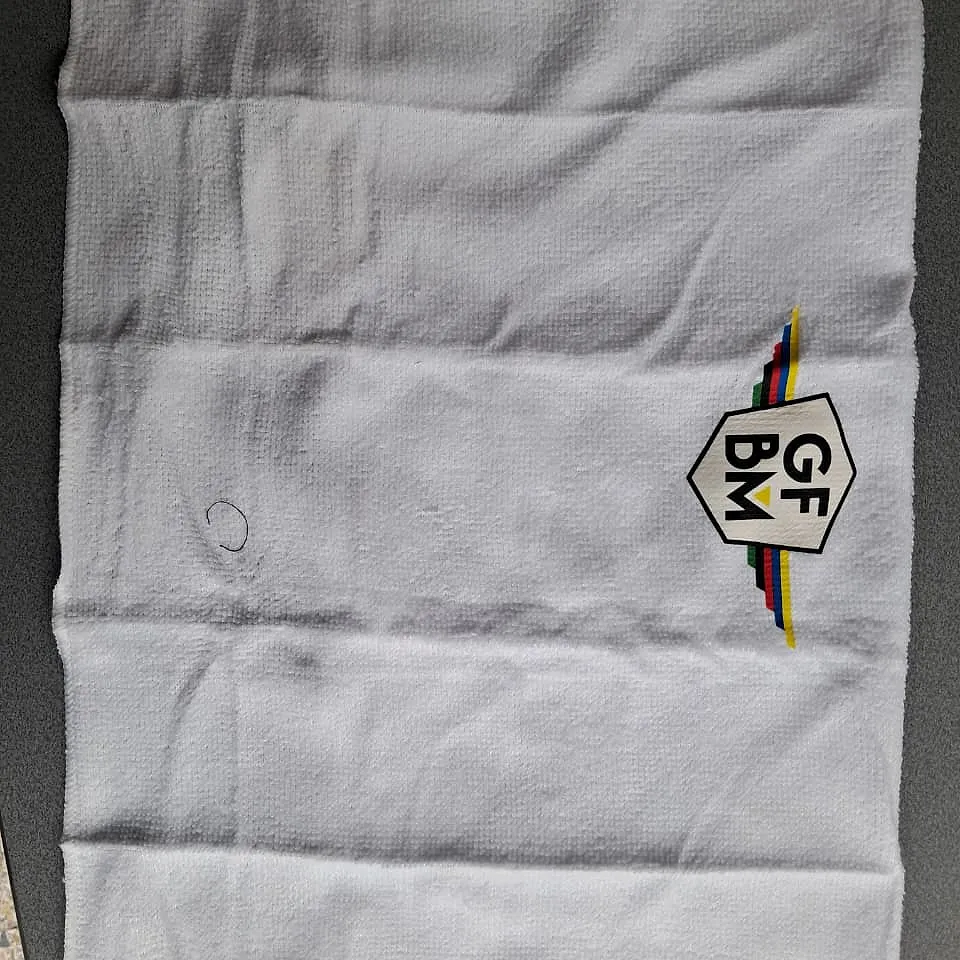 Small white GFBM towel laid flat, with the GFBM crest and the colour stripes in a corner